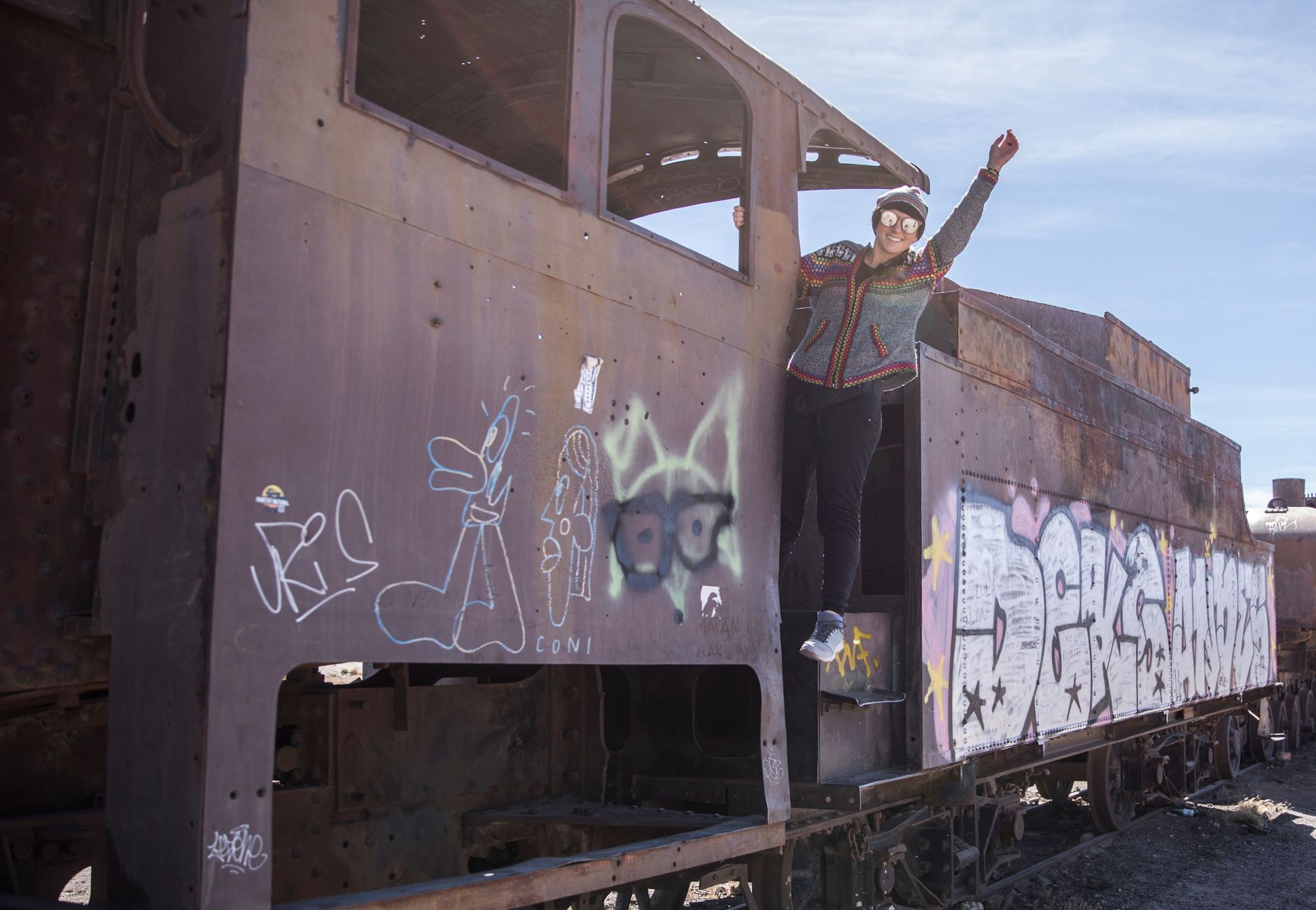 Woman posing with raised hand on an abandoned, graffiti-covered train at Uyuni's Train Graveyard, Bolivia.