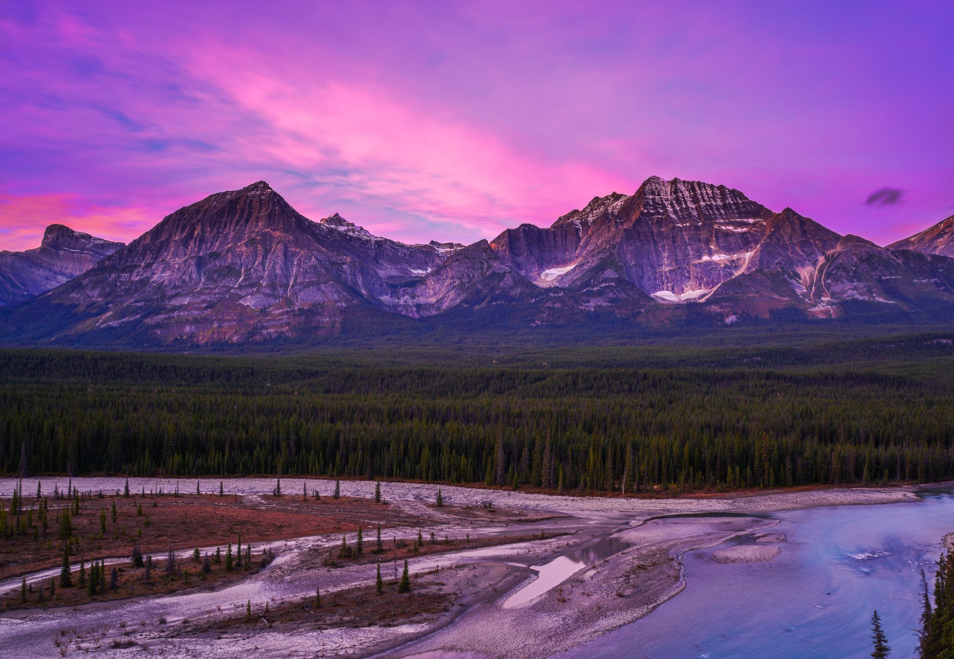 Breathtaking view of the Canadian Rockies at sunset with a vibrant purple sky.