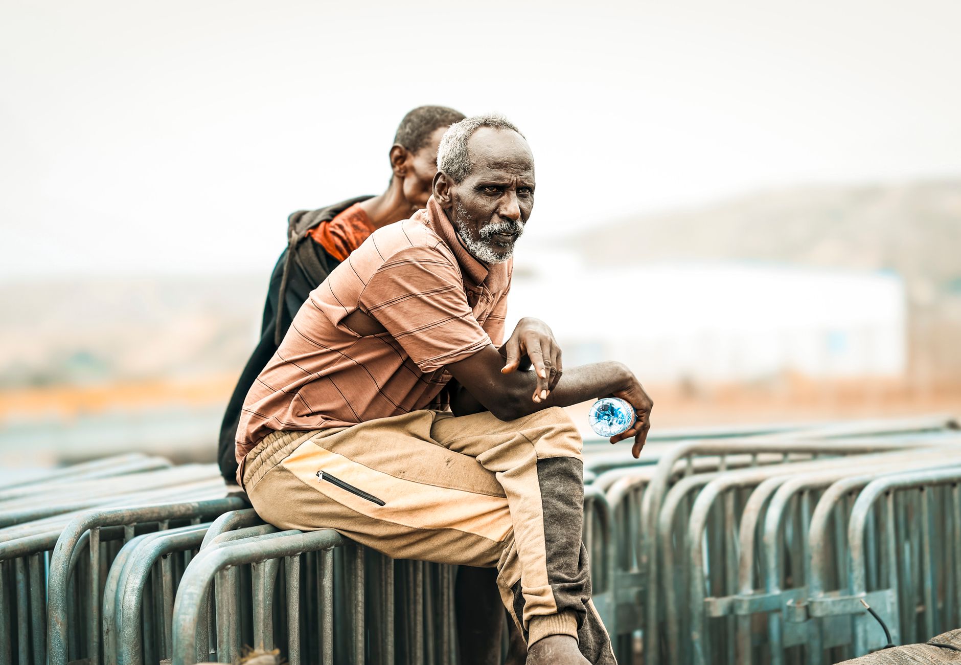 Two men sit on barriers in Tadjoura, Djibouti, with a serene background.