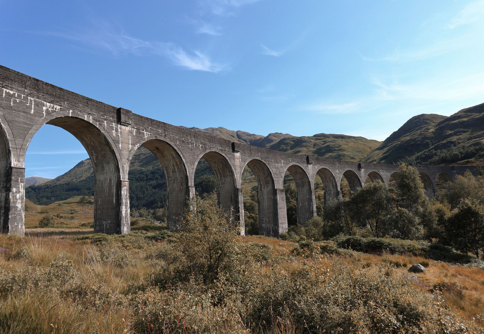 Scenic view of the iconic Glenfinnan Viaduct in the Scottish Highlands, showcasing stunning arches and lush landscape.