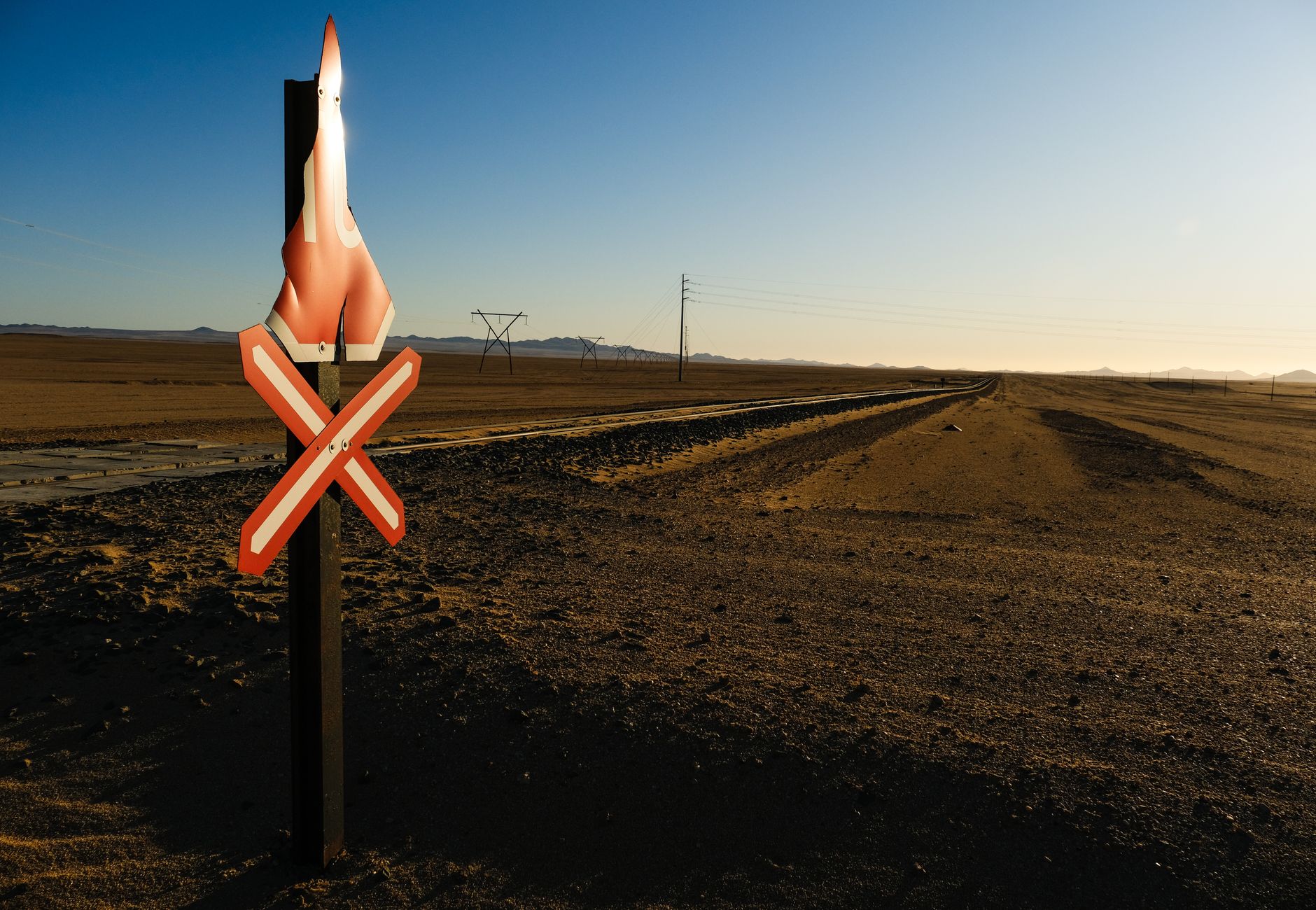Empty desert railroad scene with a warning sign, clear sky, and distant mountains.