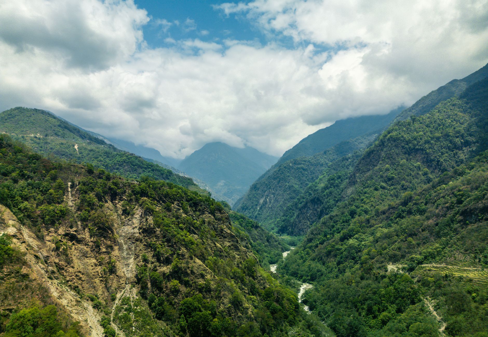 Lush green valley in Ghandruk with mountains and river under a cloudy sky in Nepal.