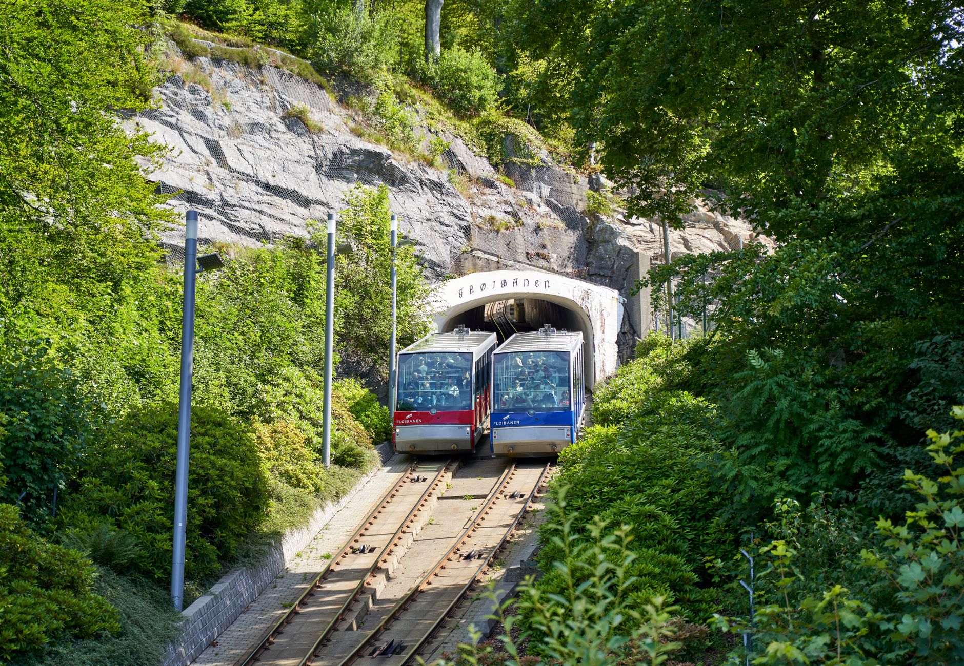 Double funiculars emerging from a tunnel in a lush green setting, Fløibanen, Bergen, Norway.