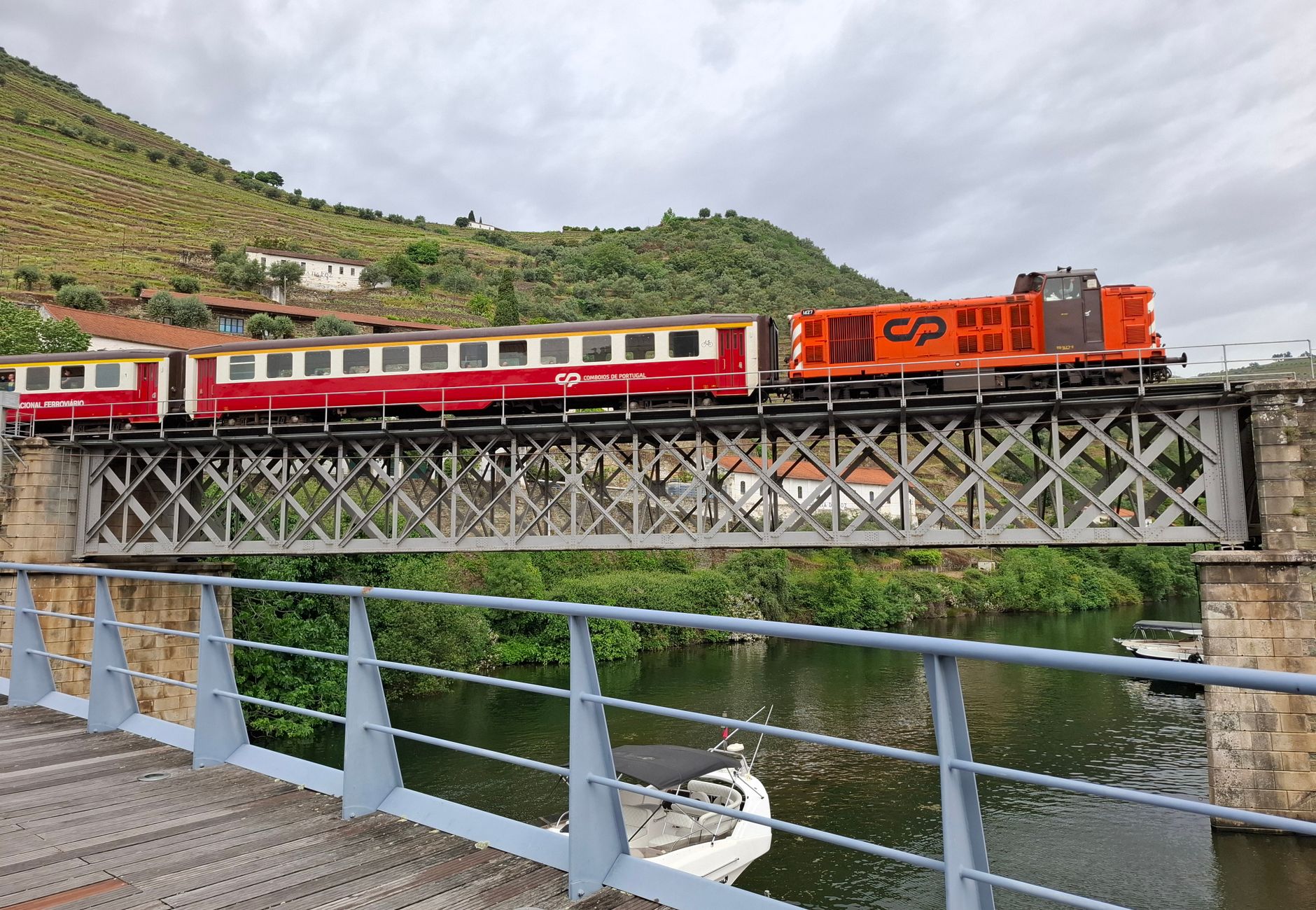 Vibrant train crossing a picturesque iron bridge over a river in Portugal's Douro Valley.