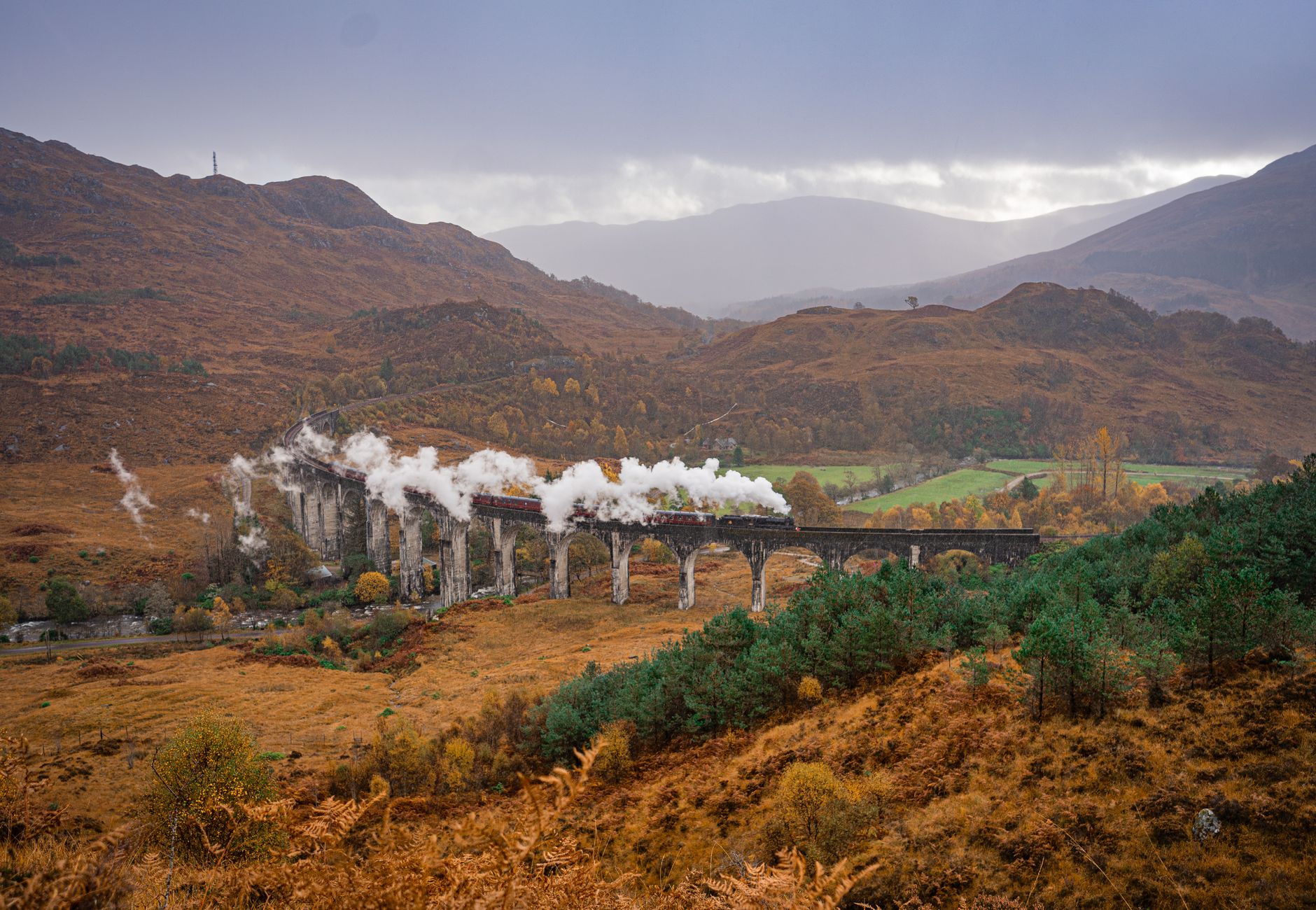 Beautiful landscape of steam train crossing Glenfinnan Viaduct in Scotland during fall.